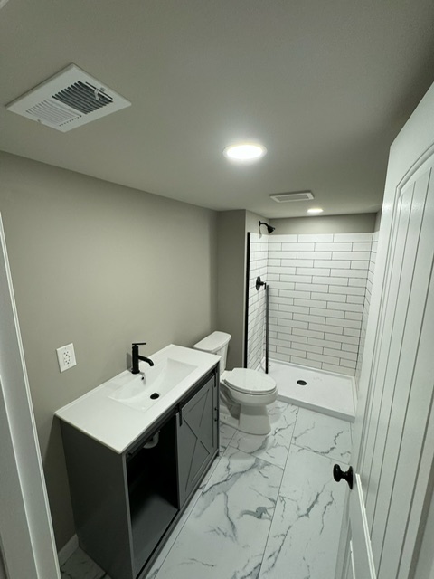 Modern bathroom remodel with walk-in shower, subway tile, marble-look flooring, and gray vanity.