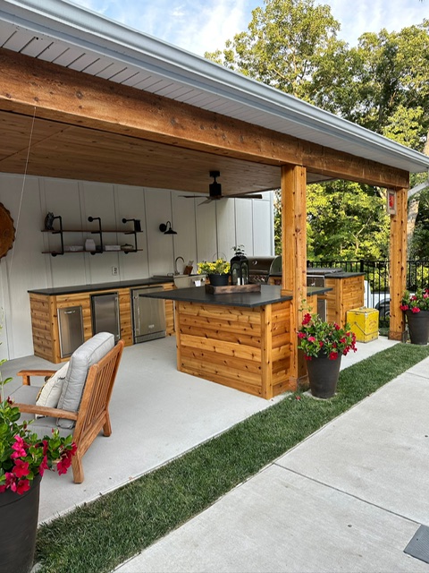 Outdoor living space featuring a covered patio with built-in kitchen, wood details, and seating area.